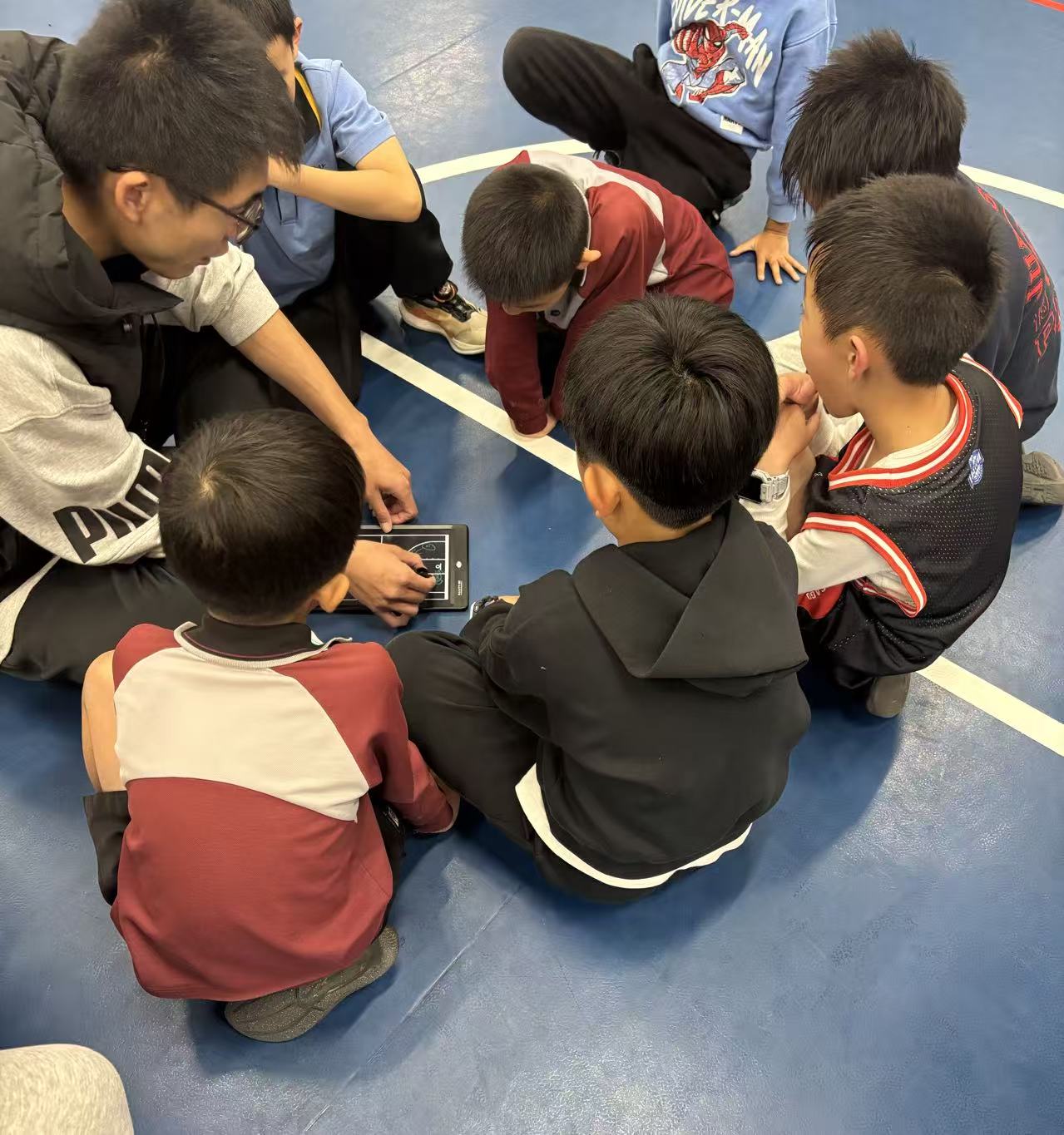 Coach explaining tactics on a tablet to a huddle of kids